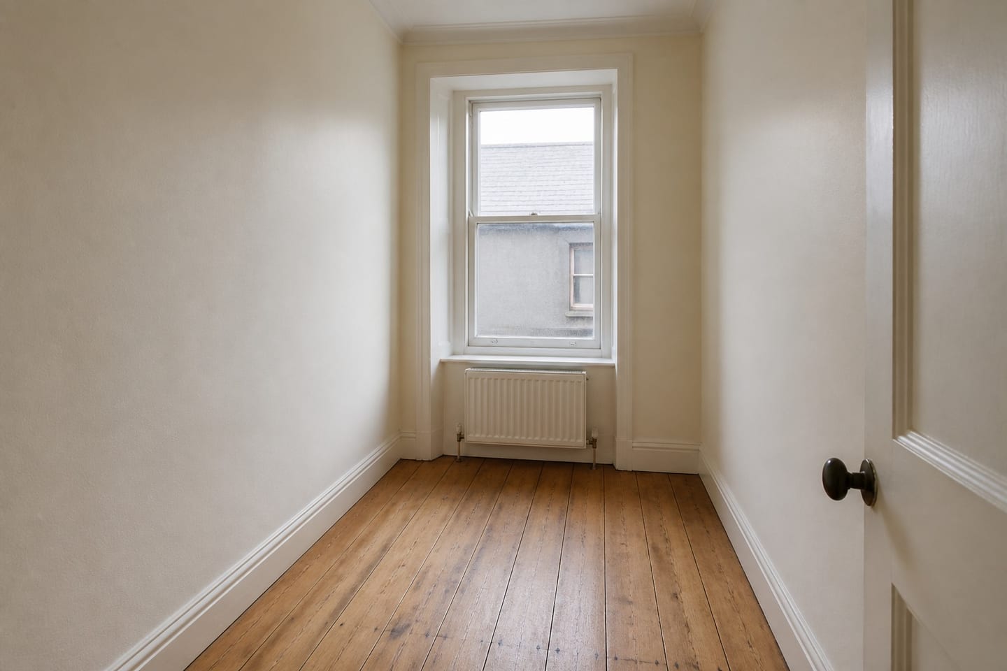 Narrow empty tenement box room with a single sash window, radiator and bare floorboards, shown before and after virtual staging with a single bed, bedside table, runner rug and a framed print — before