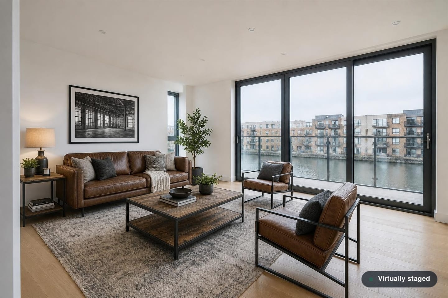 Empty waterfront new-build living room with floor-to-ceiling glazing onto a dock, shown before and after virtual staging with a tan leather sofa, steel-framed chairs and a reclaimed-wood coffee table — after