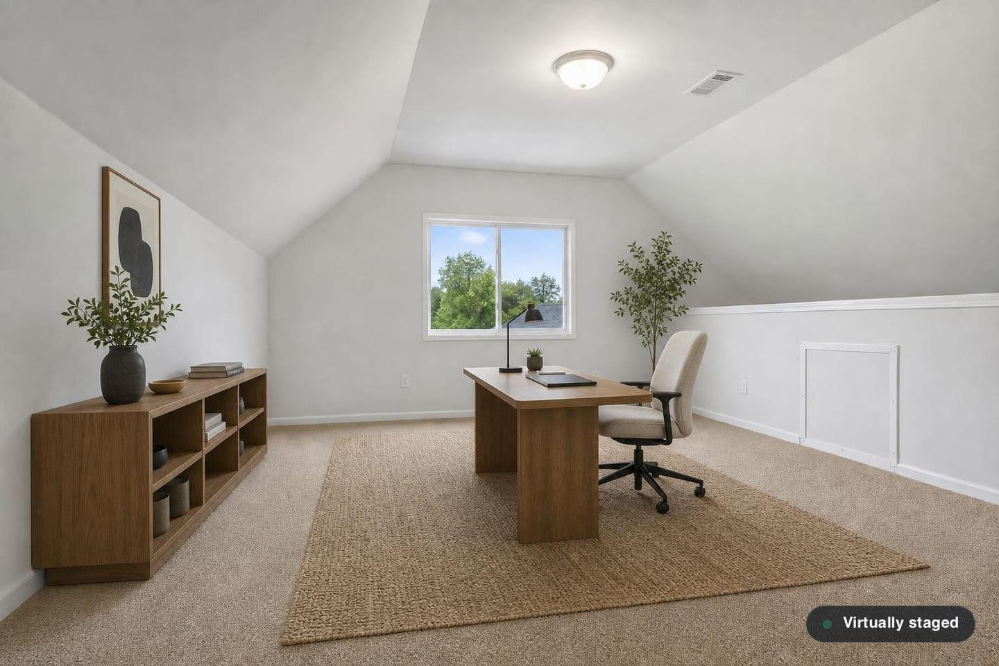 Empty bonus room over a garage with a vaulted ceiling, a knee wall with an attic access panel, a slider window in the gable end and beige carpet, shown before and after virtual staging with a desk, task chair, low bookcase and rug — after