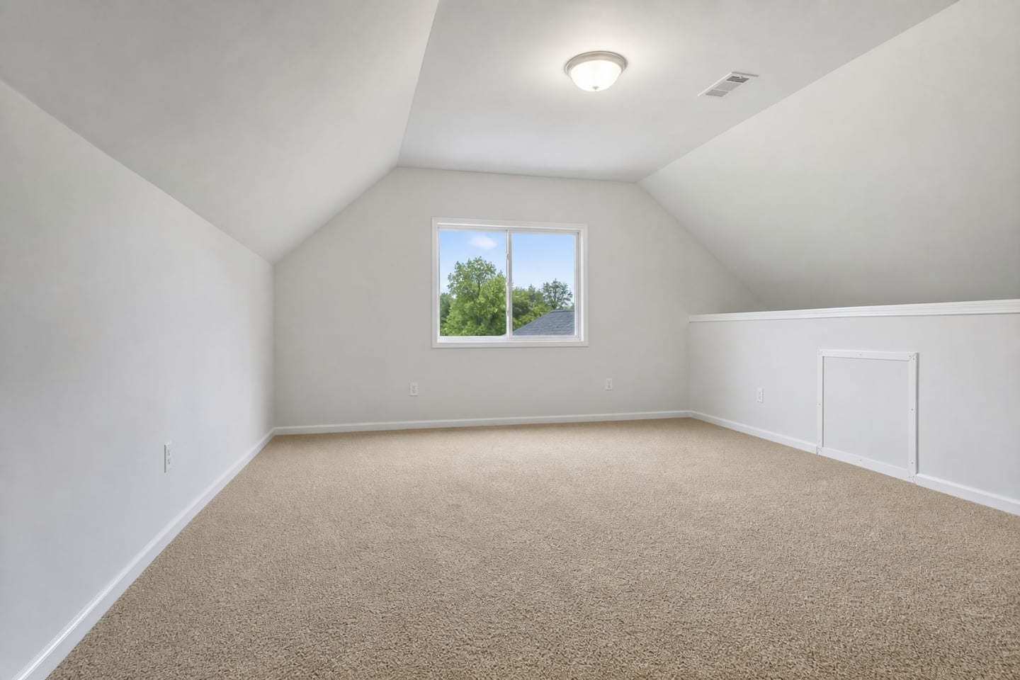 Empty bonus room over a garage with a vaulted ceiling, a knee wall with an attic access panel, a slider window in the gable end and beige carpet, shown before and after virtual staging with a desk, task chair, low bookcase and rug — before