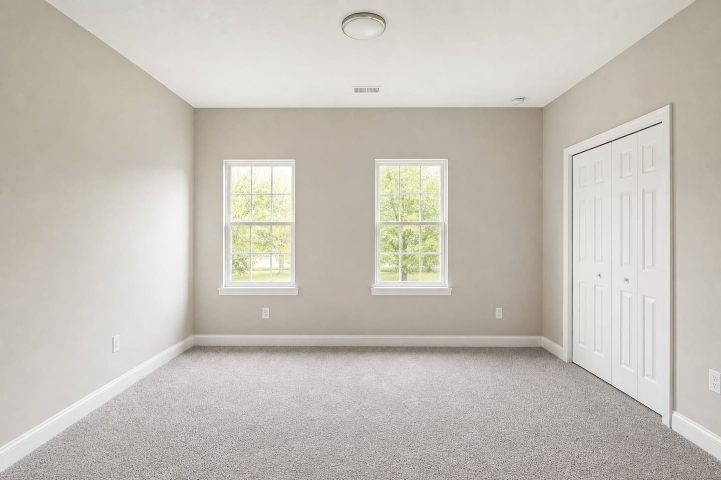 Empty American primary bedroom with two double-hung windows, a reach-in closet with white bifold doors, a ceiling register and grey carpet, shown before and after virtual staging with an upholstered bed, nightstand, lamp and jute rug — before