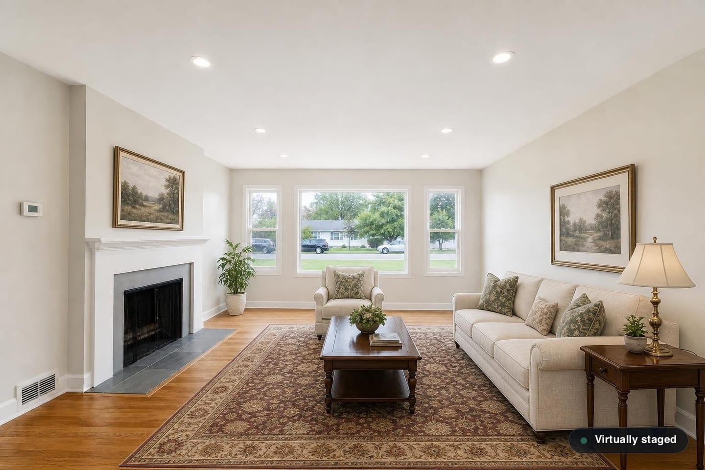 The same empty ranch front living room, shown before and after virtual staging in a Classic Traditional scheme with a rolled-arm sofa, a wing chair, a mahogany coffee table, a turned-leg side table with a brass lamp and a patterned wool rug — after